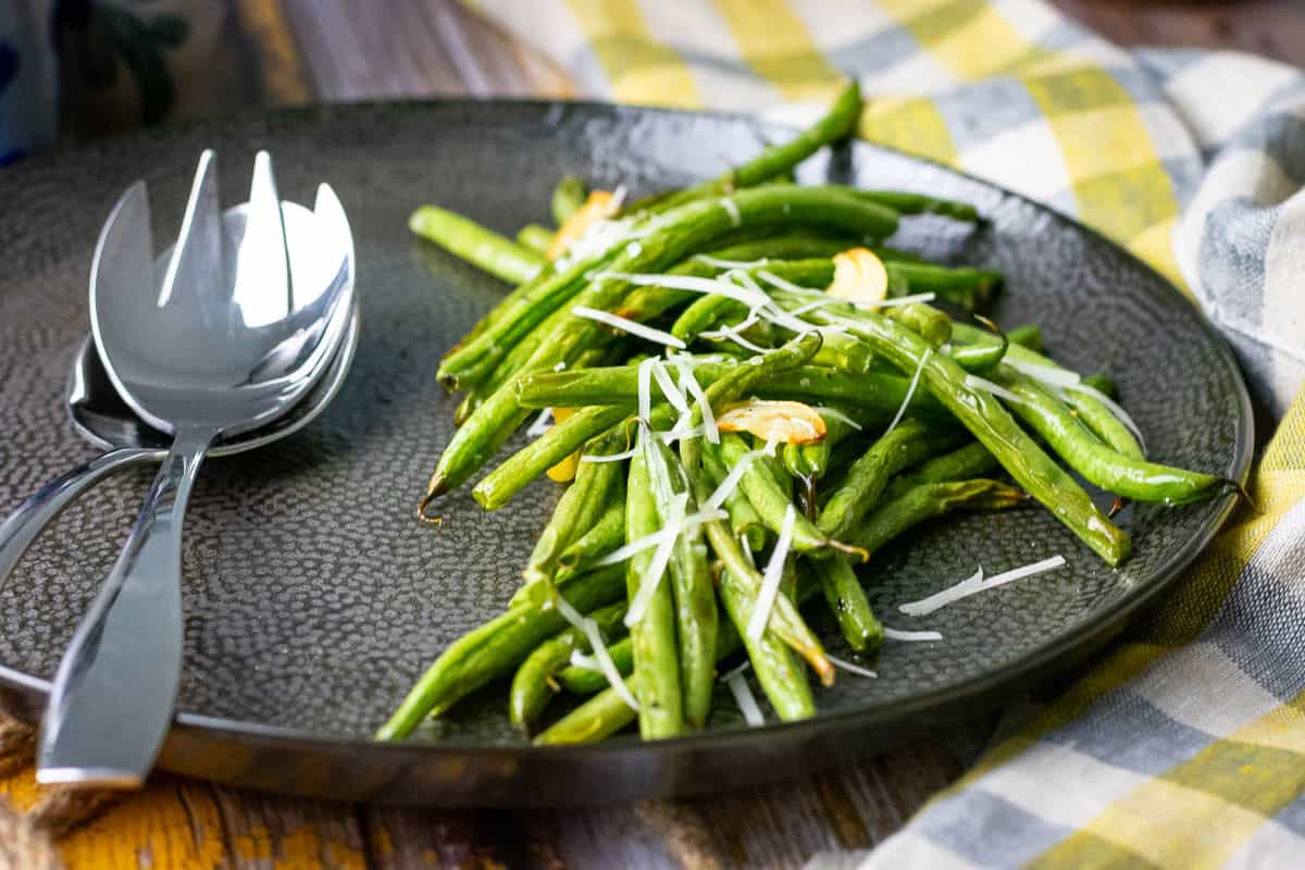 Roasted green beans with garlic, almonds and parmesan on a black plate.