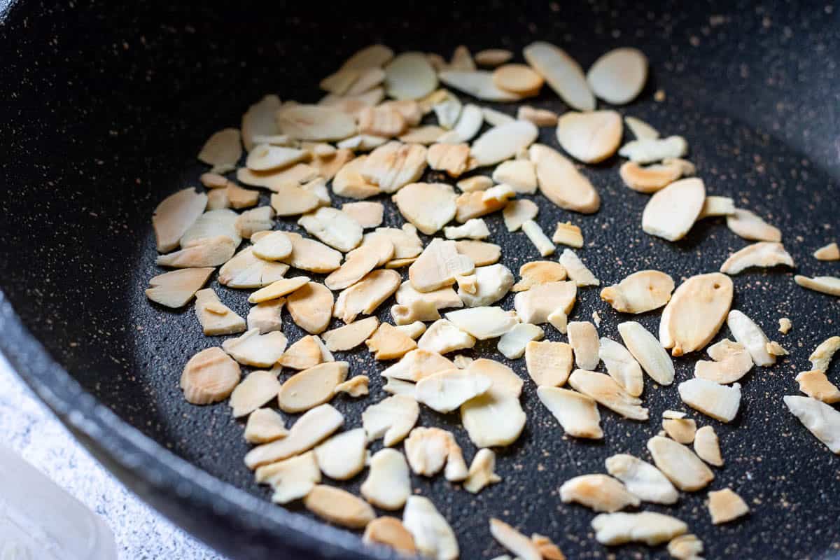 Flaked almonds toasting in a frying pan.