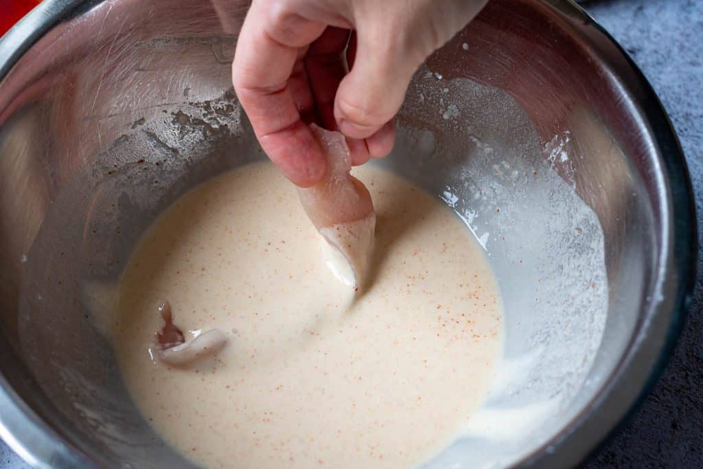 A thick strip of chicken being dipped in the batter.