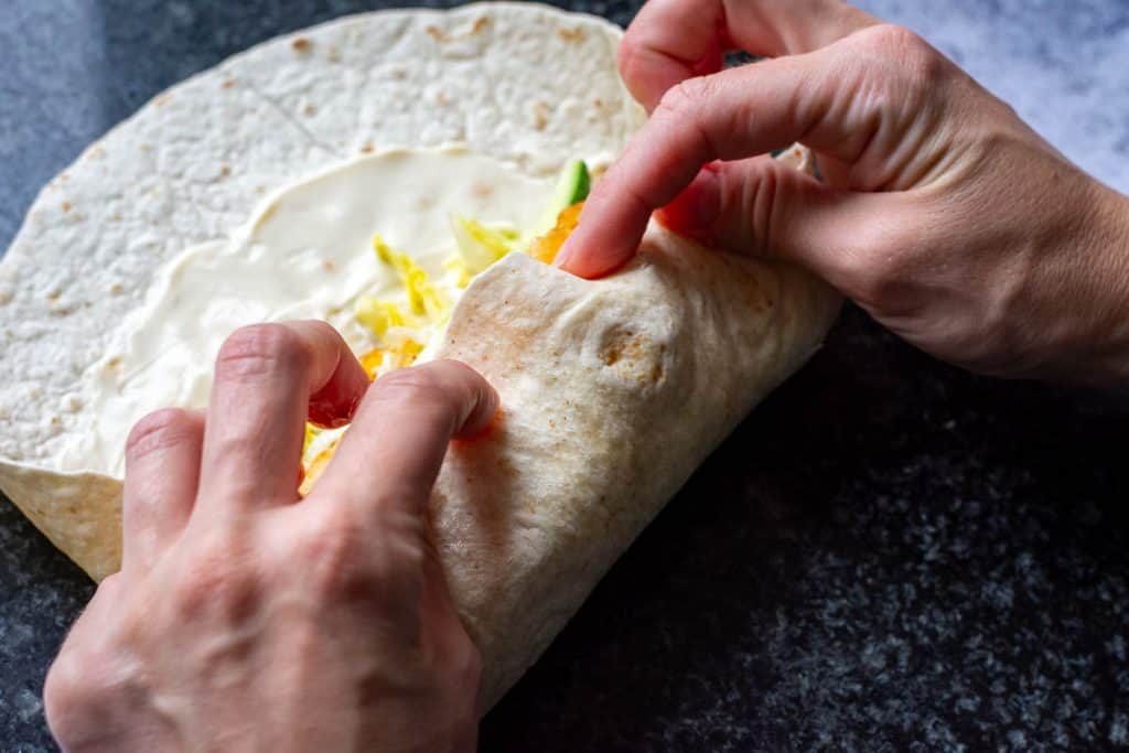 Rolling the tortilla to encase hot honey chicken filling.