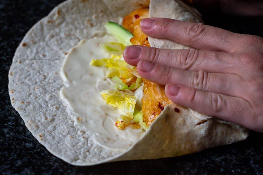 Rolling the tortilla to encase hot honey chicken filling.