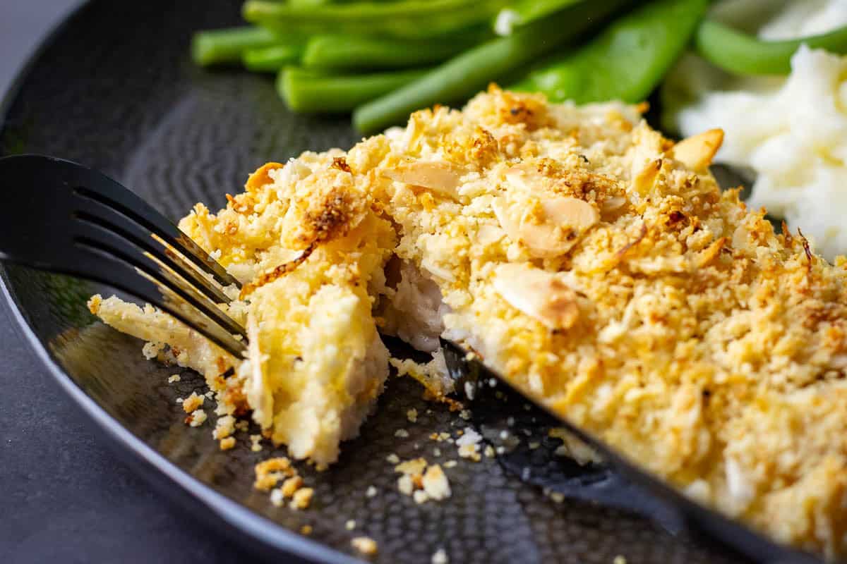 A piece of almond crusted fish being cut.