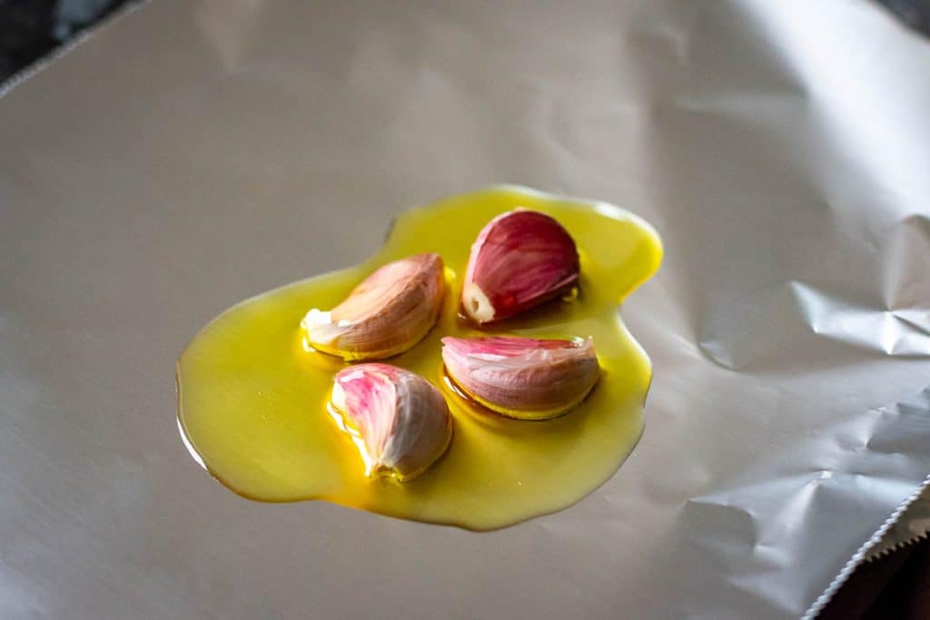 Garlic cloves with olive oil on a piece of aluminium foil.