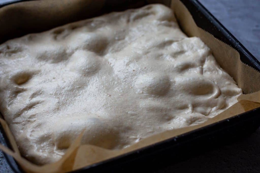 Sourdough focaccia dough stretched into a square high-rimmed baking tray.