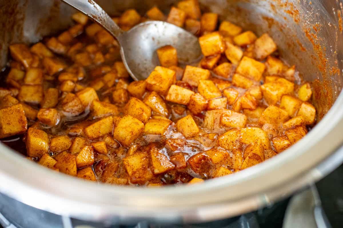 Stewed cinnamon apples in a pan being stirred with a spoon.