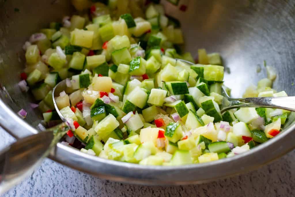 Tossing the cucumber pineapple salad wth the dressing in a metal mixing bowl.