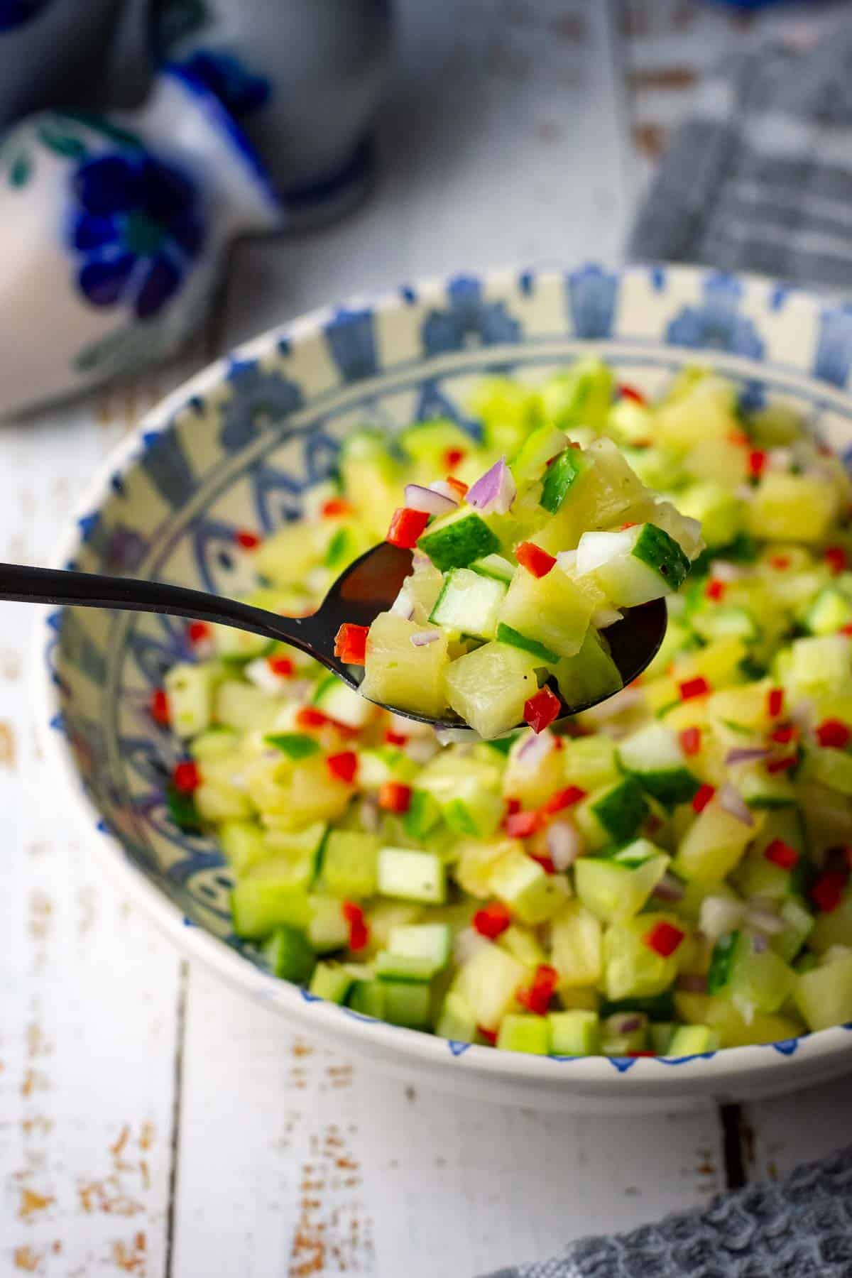 A spoonful of cucumber and pineapple salad lifted out of the bowlful of it.