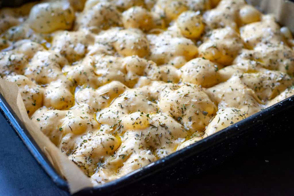 Sourdough pumpkin focaccia dough sprinlled with dried herbs and salt.