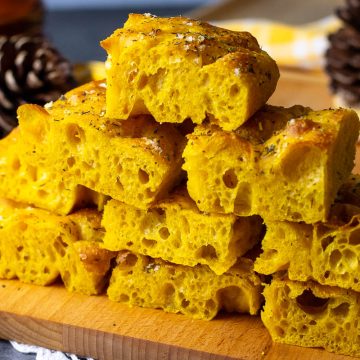 Pumpkin Sourdough Focaccia cut into sqares and stacked on a wooden board.