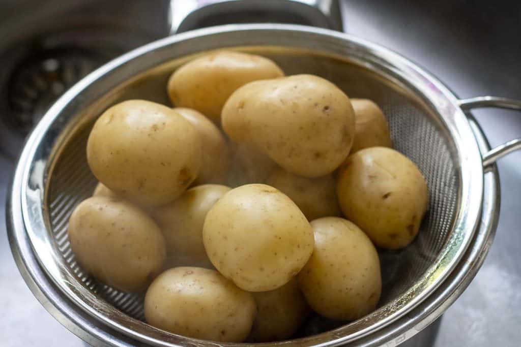 Boiled baby potatoes steaming in colander.