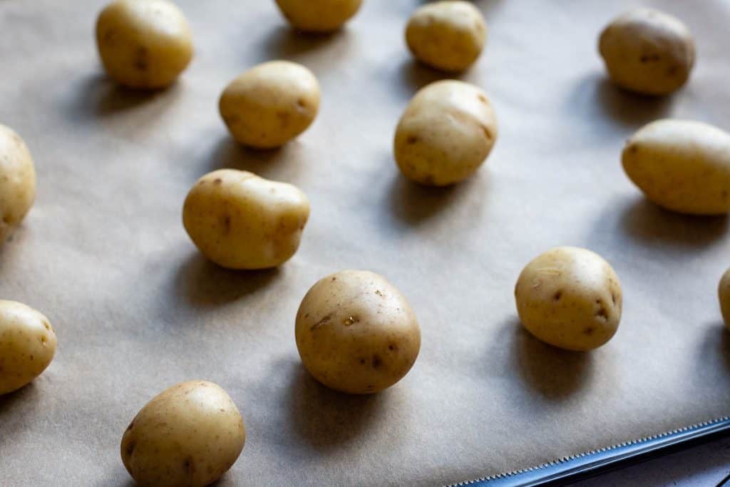Cooked baby potatoes arrange don a large baking sheet lined with parchment paper.