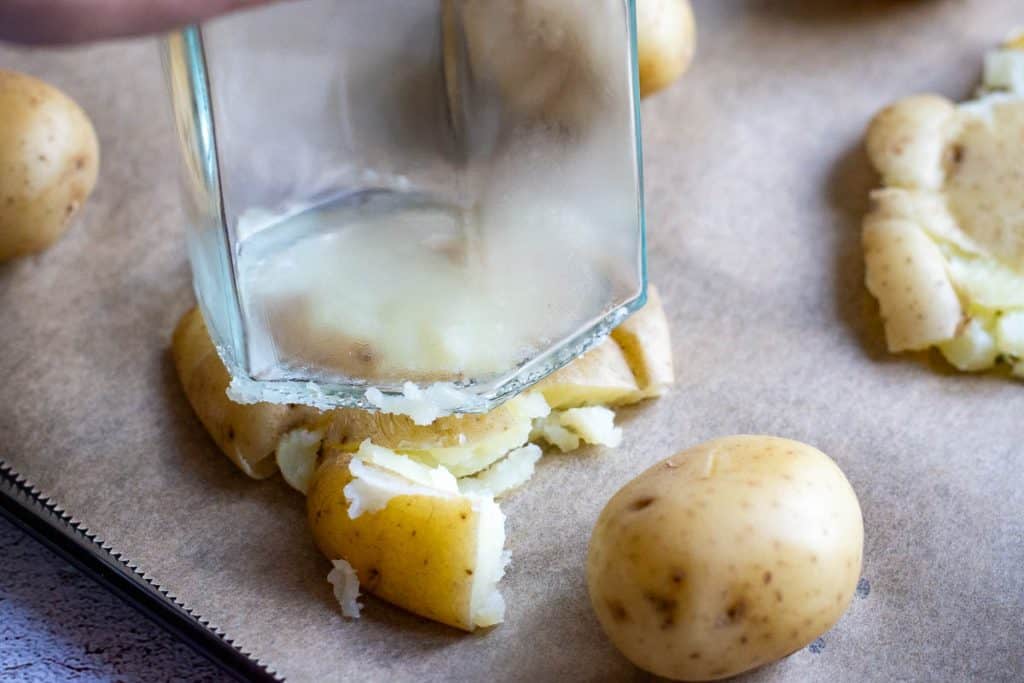 Smashing the pottaoes flat on the parchment paper using the base of a glass jar.