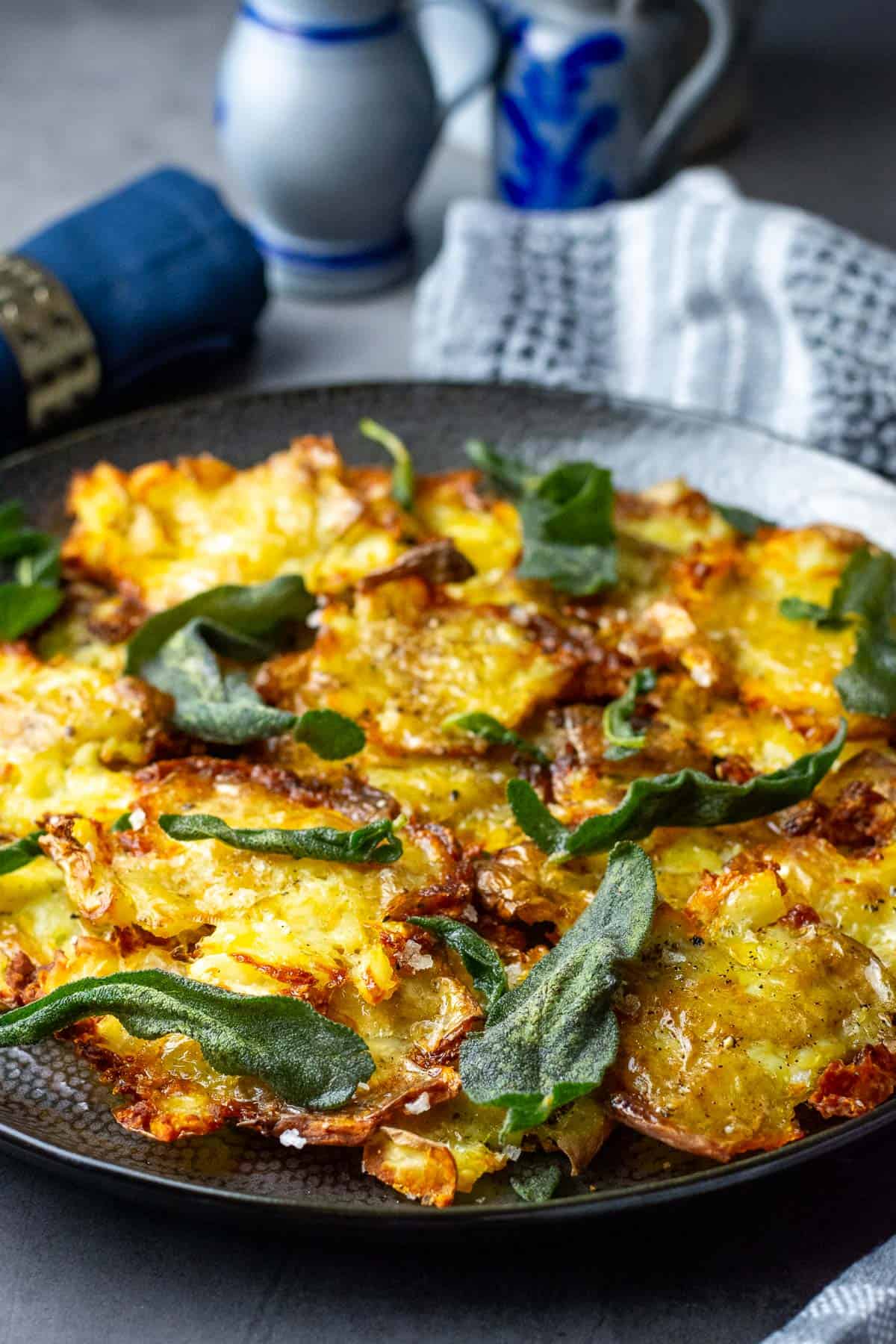 Crispy Smashed Sage Potatoes on a black plate topped with sage butter and crispy sage leaves.