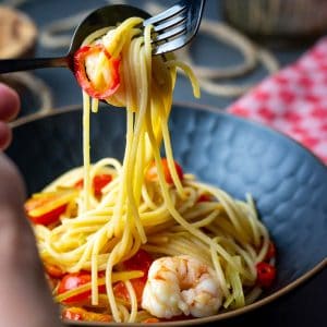 Fennel and prawn spaghetti being picked up from a black bowl by a fork.