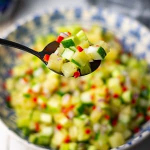 A spoonful of cucumber and pineapple salad lifted out of the bowlful of it.