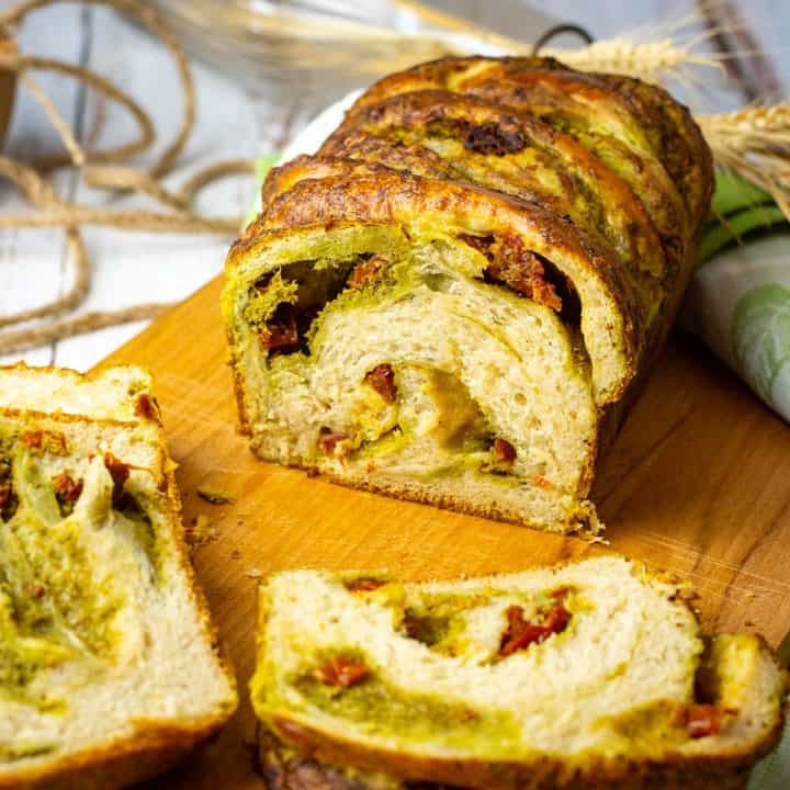 Savoury sourdough babka with pesto and sundried tomatoes sliced on a wooden board.
