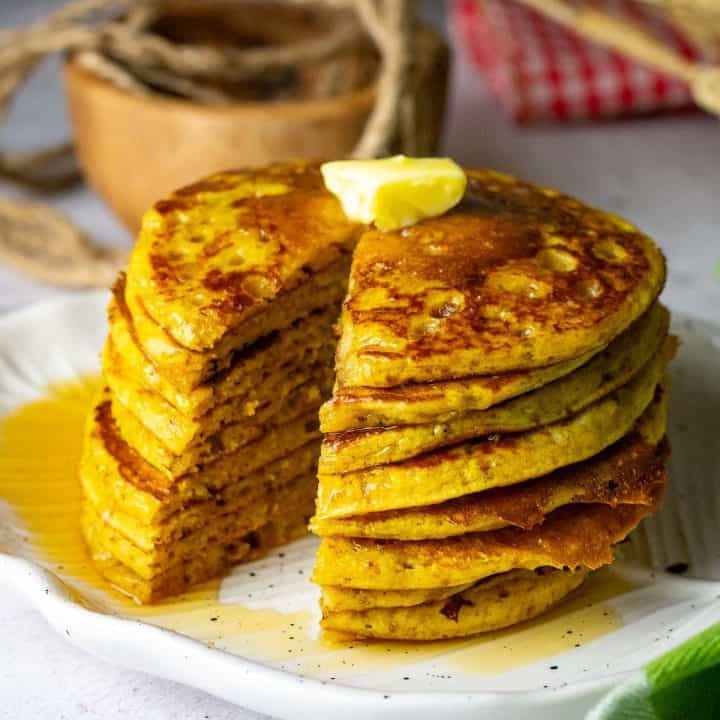 A stack of sourdough pumpkin pancakes on a white plate with maple syrup and butter on top.