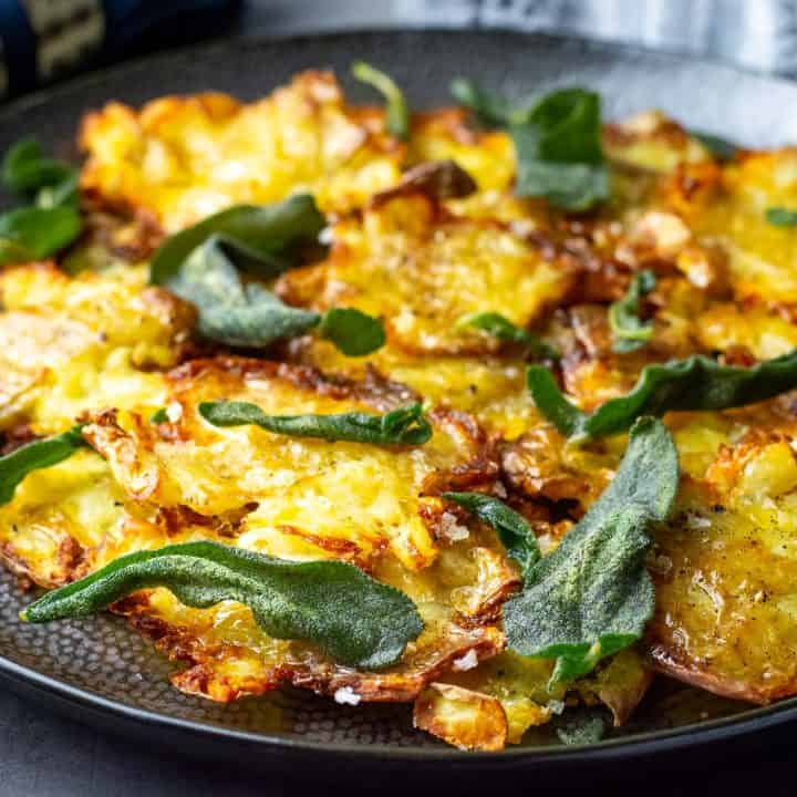 Crispy Smashed Sage Potatoes on a black plate topped with sage butter and crispy sage leaves.