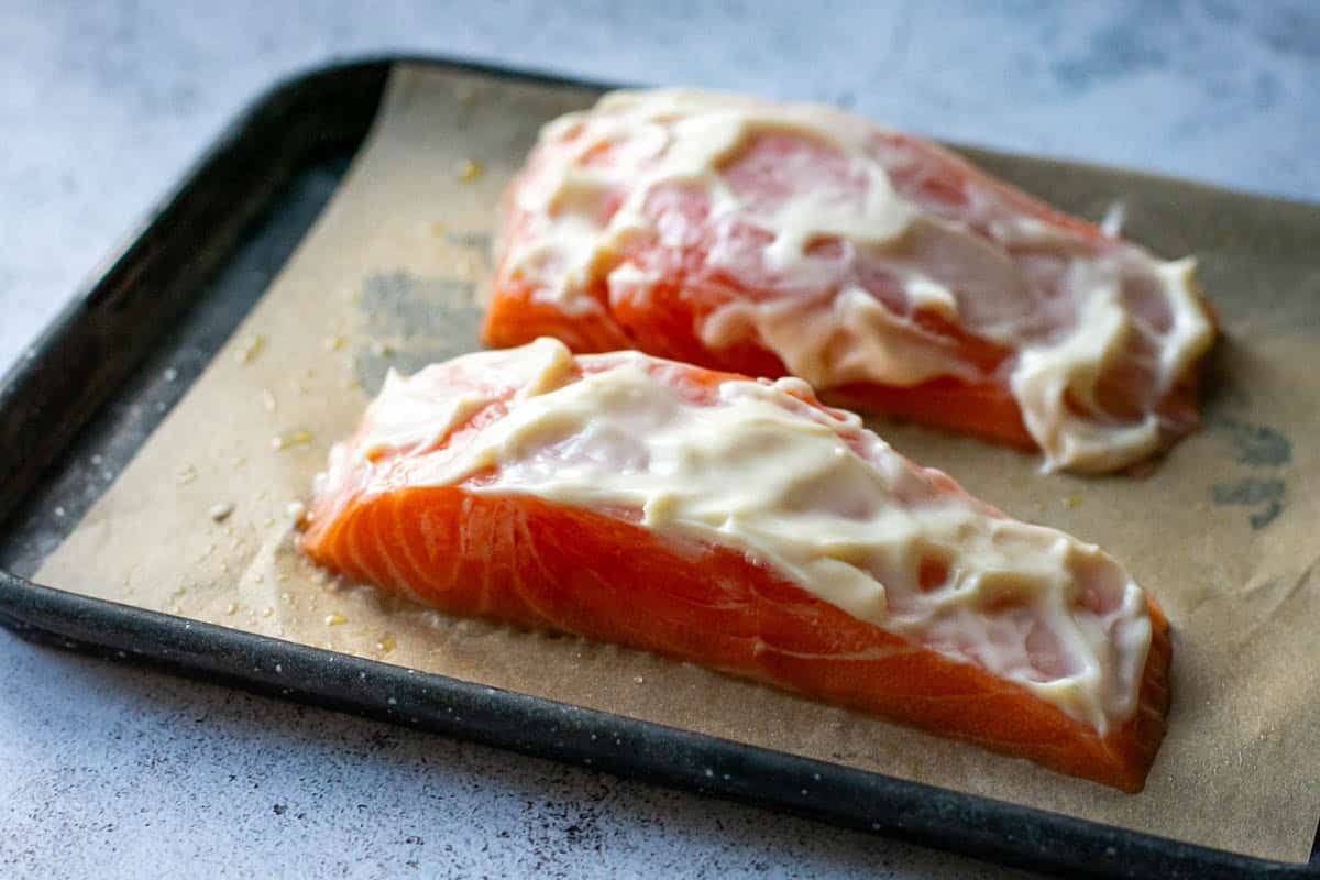 Two salmon fillets with mayonnaise spread on top.