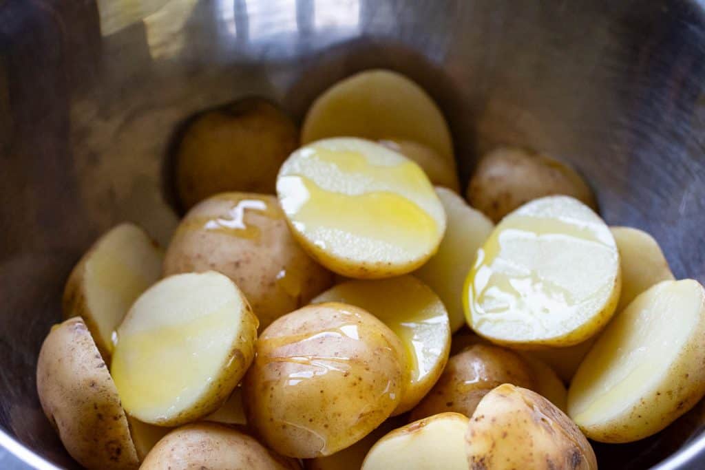 Halved baby potatoes with oil in a large metal bowl.