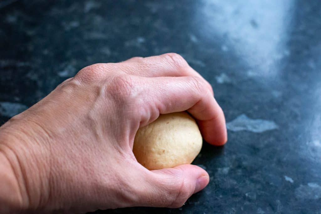 Cupping a a ball of pumpkin sourdough and rolling it against kitchen surface to create tension.