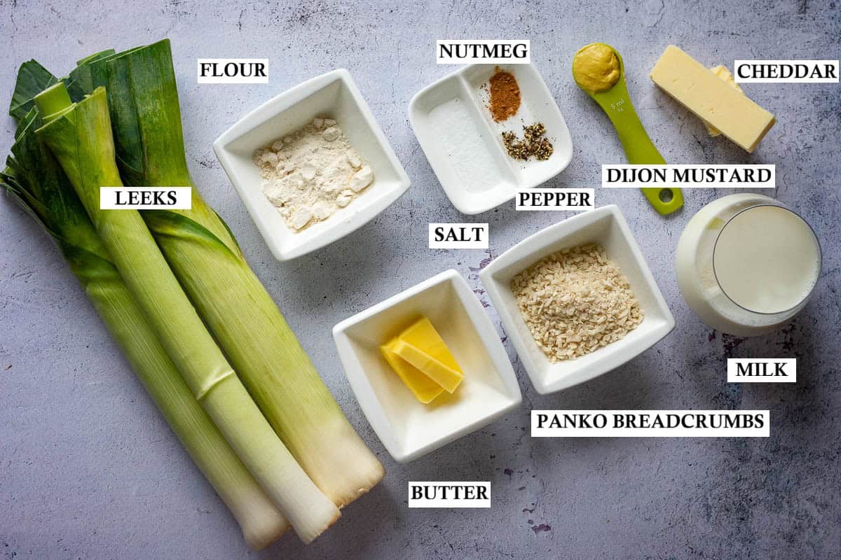 Ingredients for Cheesy Leeks baked in creamy sauce on light grey surface.