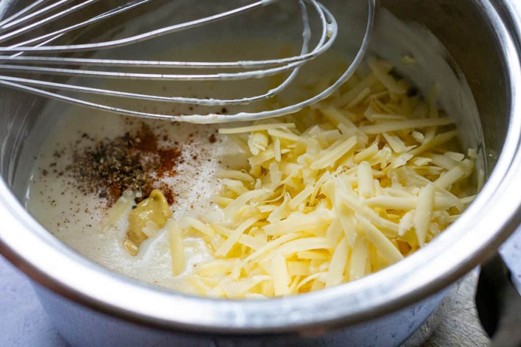 Adding grated cheese, mustard and nutmeg to the white sauce.