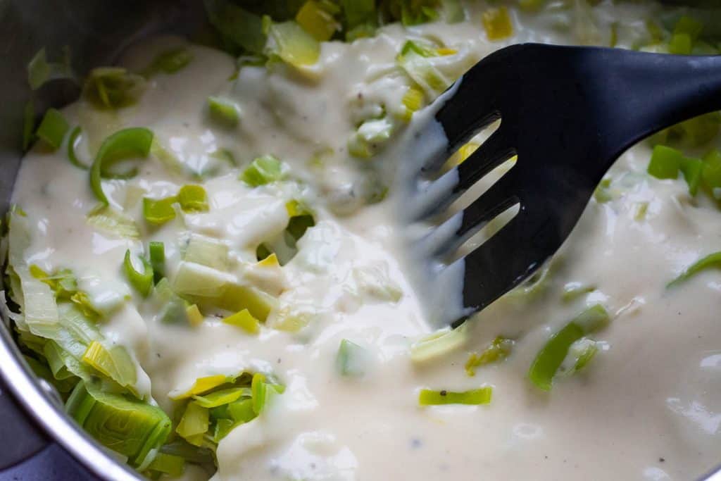 Stirring sauteed leeks with white sauce.