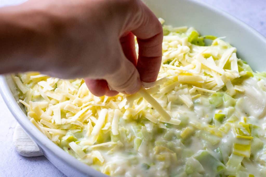 Topping creamy leeks with grated cheese.