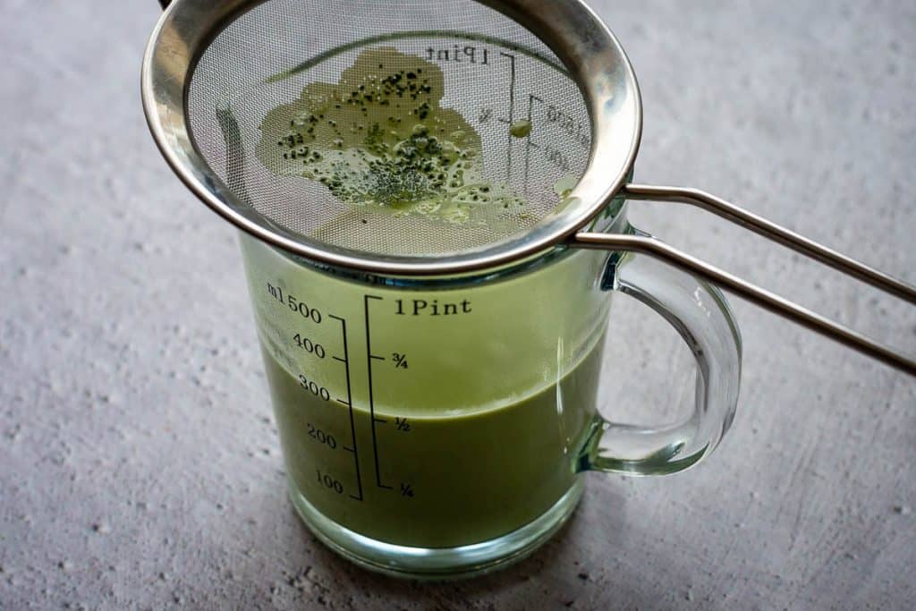 matcha cream mixture poured through a fine sieve into a glass jug.