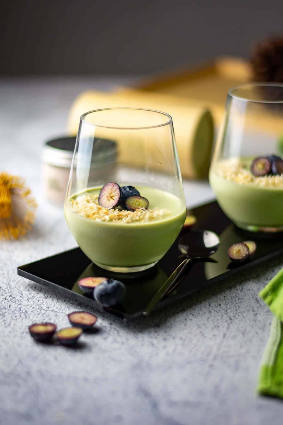 Two glasses of matcha panna cotta topped with toasted coconut and blueberries.