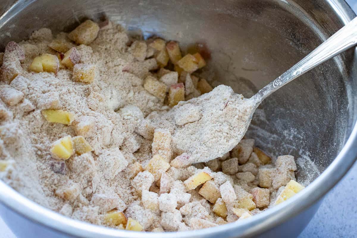 Apple cubed mixed with dry ingredients in a large metal bowl.