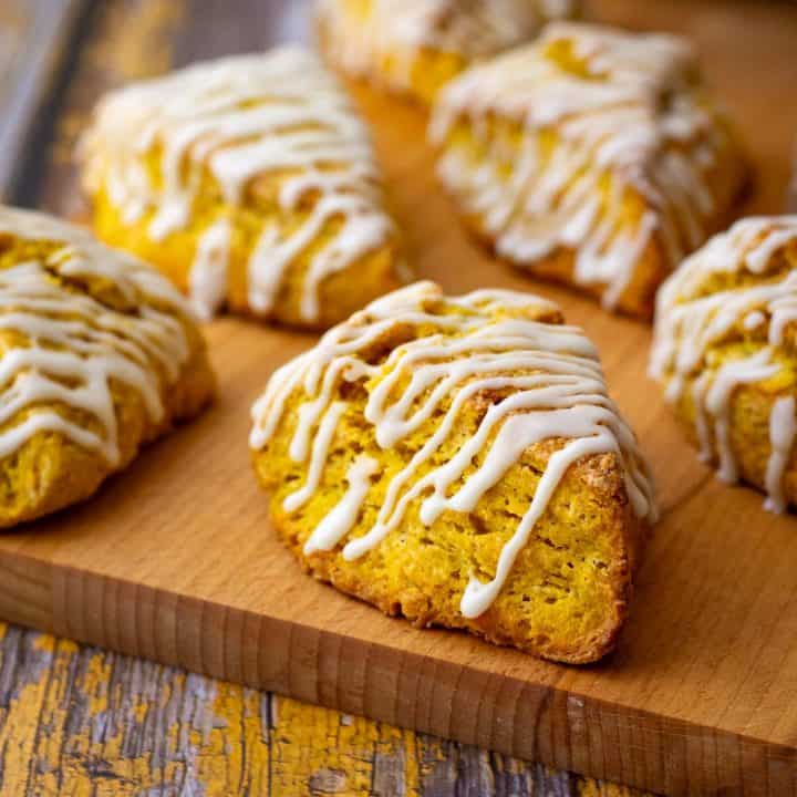 Sourdough Pumpkin Scones with maple glaze on a parchment lined wooden board.