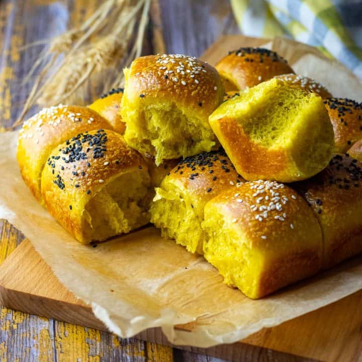Sourdough Pumpkin Dinner rolls on a wooden board with two of them pulled apart showing soft and fluffy interior.