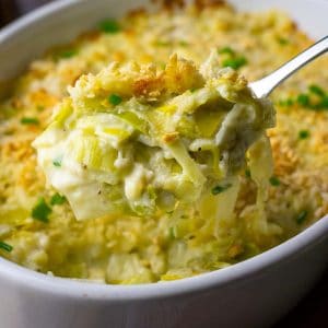 A spoonful of creamy cheesy leeks being lifted out of a casserole dish.