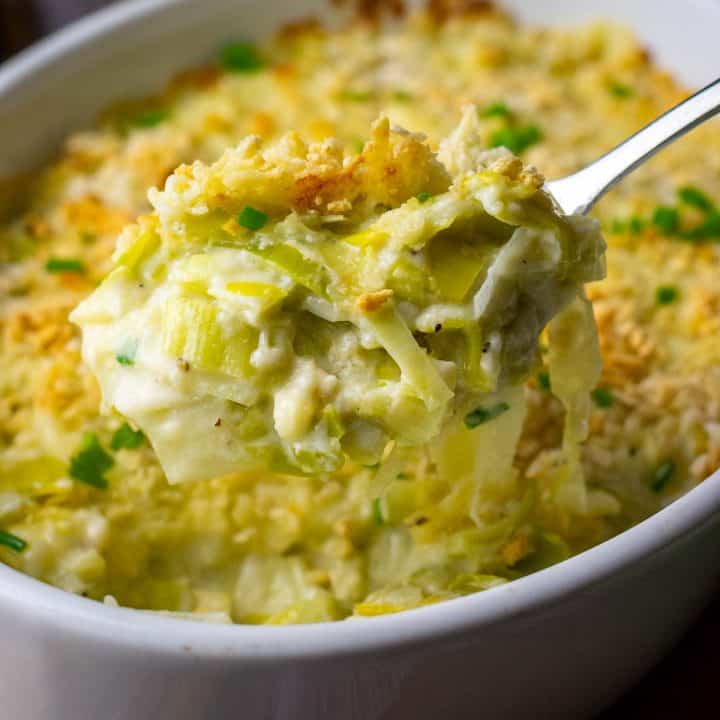 A spoonful of creamy cheesy leeks being lifted out of a casserole dish.