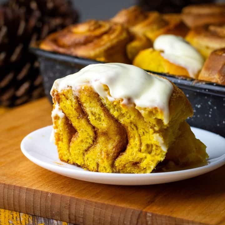 Sourdough pumpkin cinnamon roll cut in half on a plate.