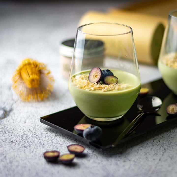 Two glasses of matcha panna cotta topped with toasted coconut and blueberries.