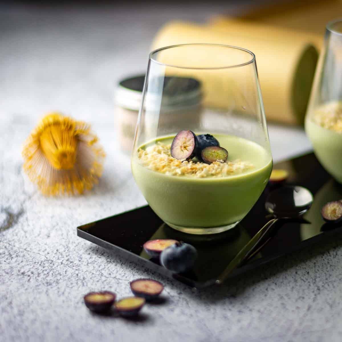 Two glasses of matcha panna cotta topped with toasted coconut and blueberries.