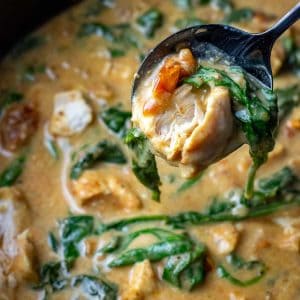 A spoonful of slow cooker Tuscan chicken liften out of the slow cooker bowl.