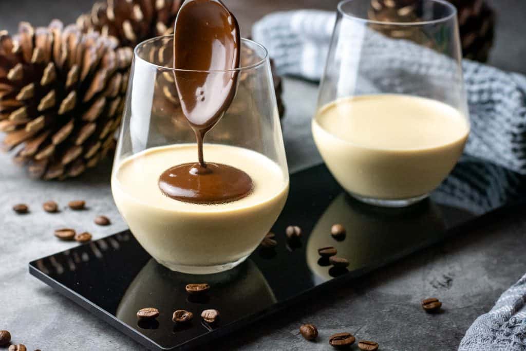 Spooning dark chocolate sauce on top of set espresso panna cottas.