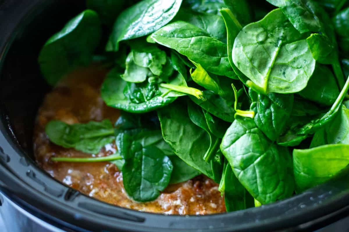 Spinach being added to slow cooker Tuscan chicken.