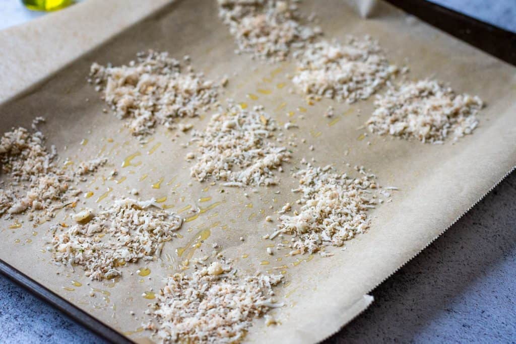 Circles of parmesan mixture sprinlled on an oiled baking parchment.