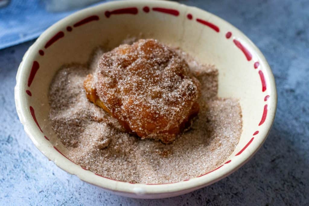 Sourdough apple fritter in a bowl with cinnamon sugar.