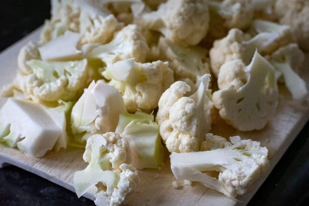 Cauliflower cut into florets on a wooden chopping board.
