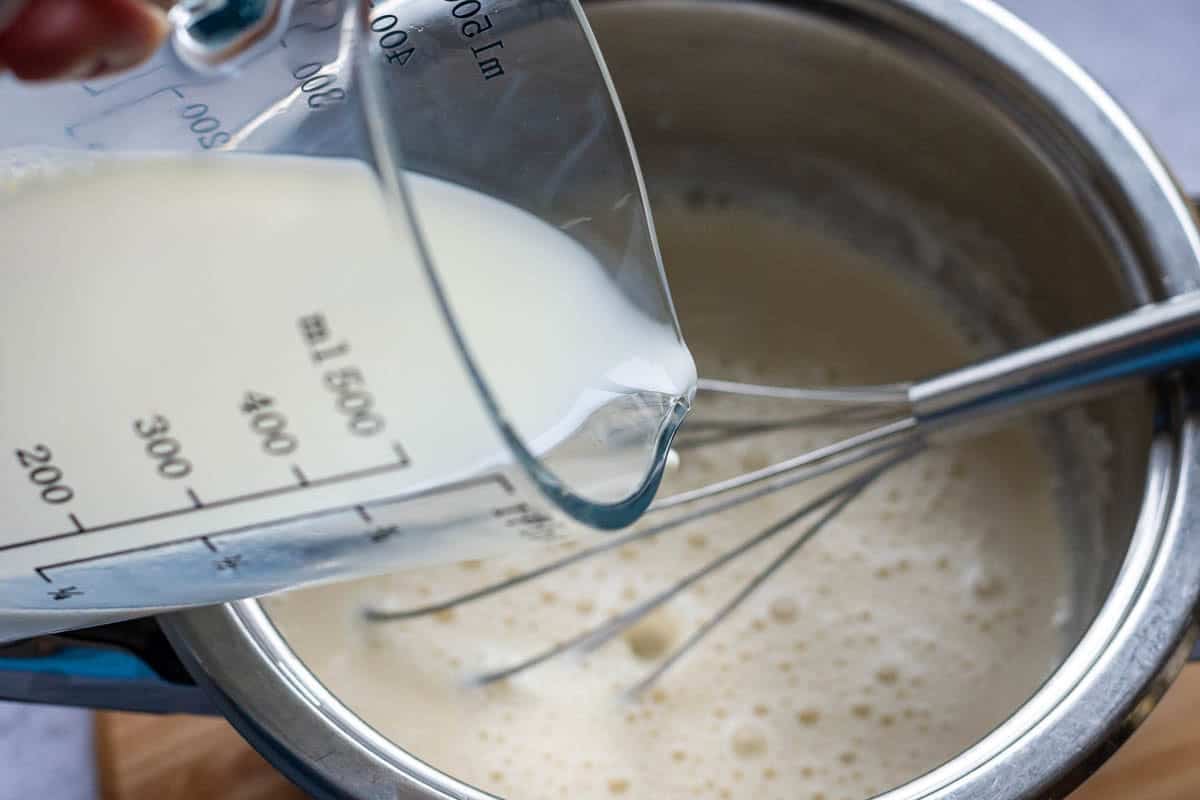 Milk being poured into sourdough discard roux to make white sauce for cauliflower cheese.
