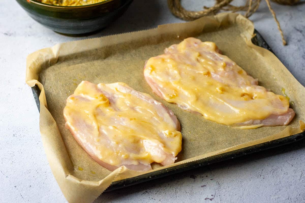 Chicken breasts on a baking tray lined with parchment paper with mango chutney and mayo spread on top of each.