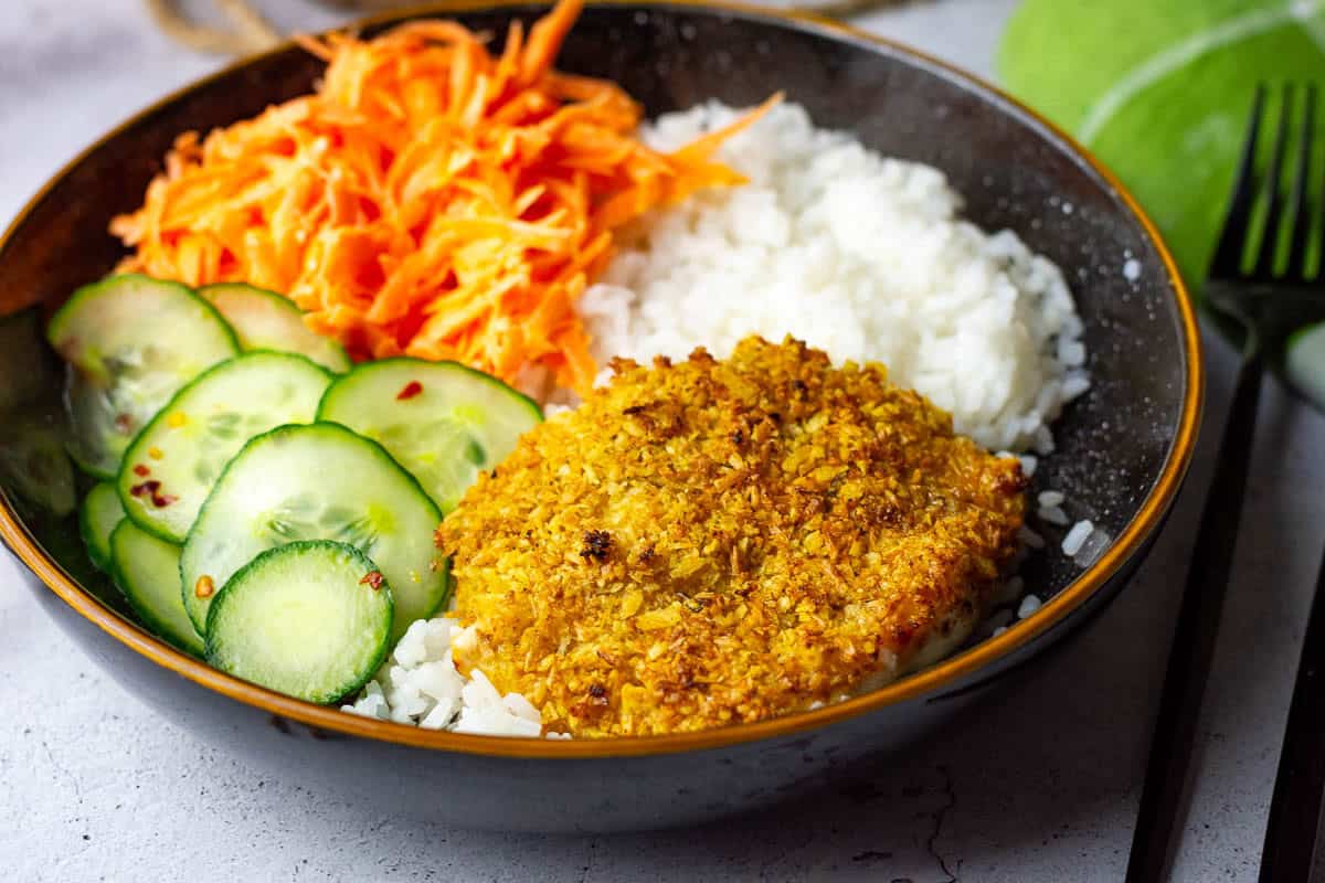 Baked Coconut Crusted Chicken breast on a bed of rice with vegetables.