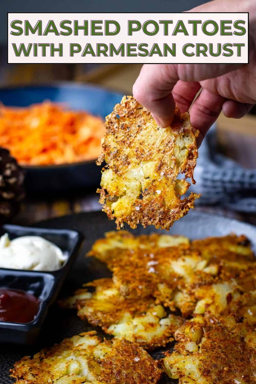Parmesan Smashed Potatoes on a black plate with one being picked up - Pin for Pinterest.