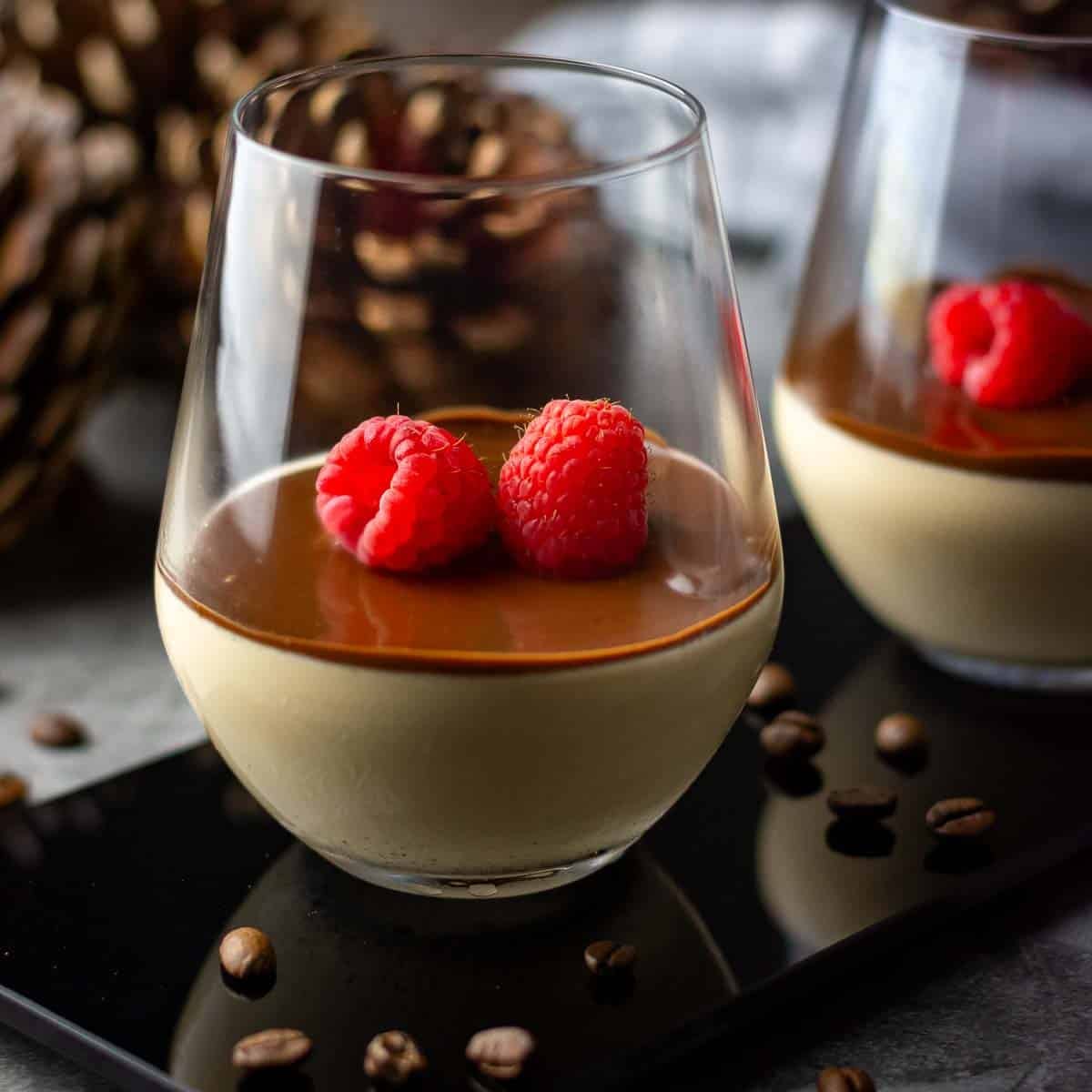 Two glasses of espresso panna cotta with chocolate sauce and raspberries on top.